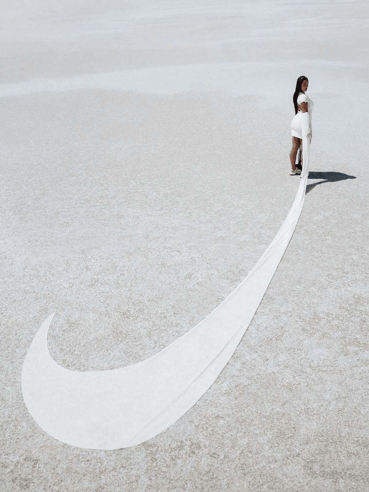 A Nike × Jacquemus campaign image of a model with a fabric train forming a swoosh